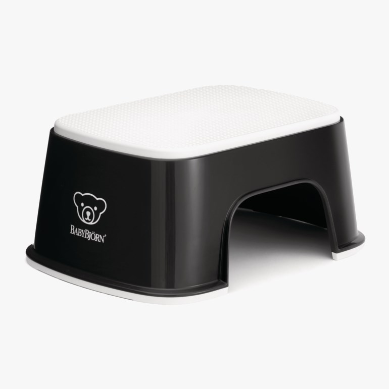 Svart og hvit plastkrakk med strukturert toppflate og avrundede kanter, forfra.