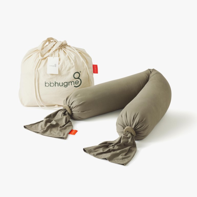 Olivengrønn U-formet graviditetspute med stoffbånd og treringer, ved siden av en beige stoffpose med snøring.