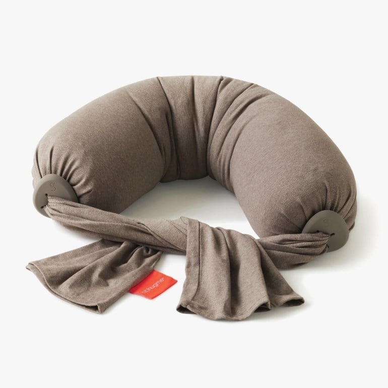 Brun U-formet multifunksjonspute med grå fester og en festet matchende stoffrem med rød etikett.