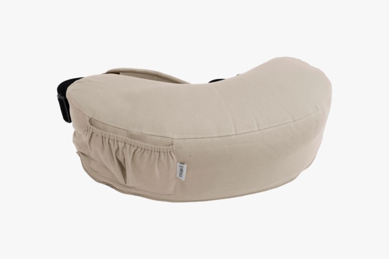 En lys beige halvmåneformet ammepute med en liten sidelomme og stoffetikett, sett fra en vinklet vinkel.