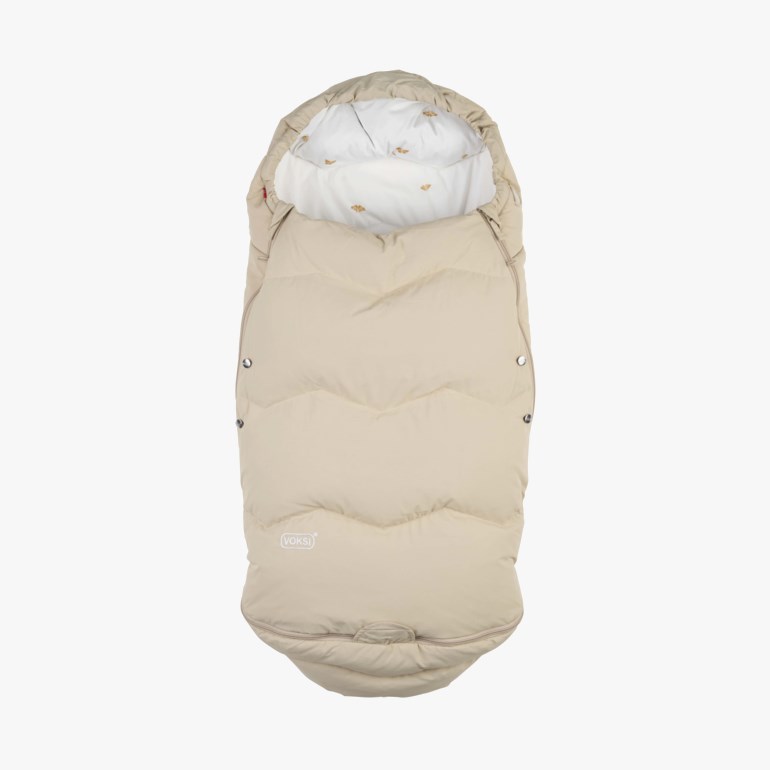 Lys beige polstret babyliggepose med hette, hvitt mønstret fôr og trykknapper i sidene.