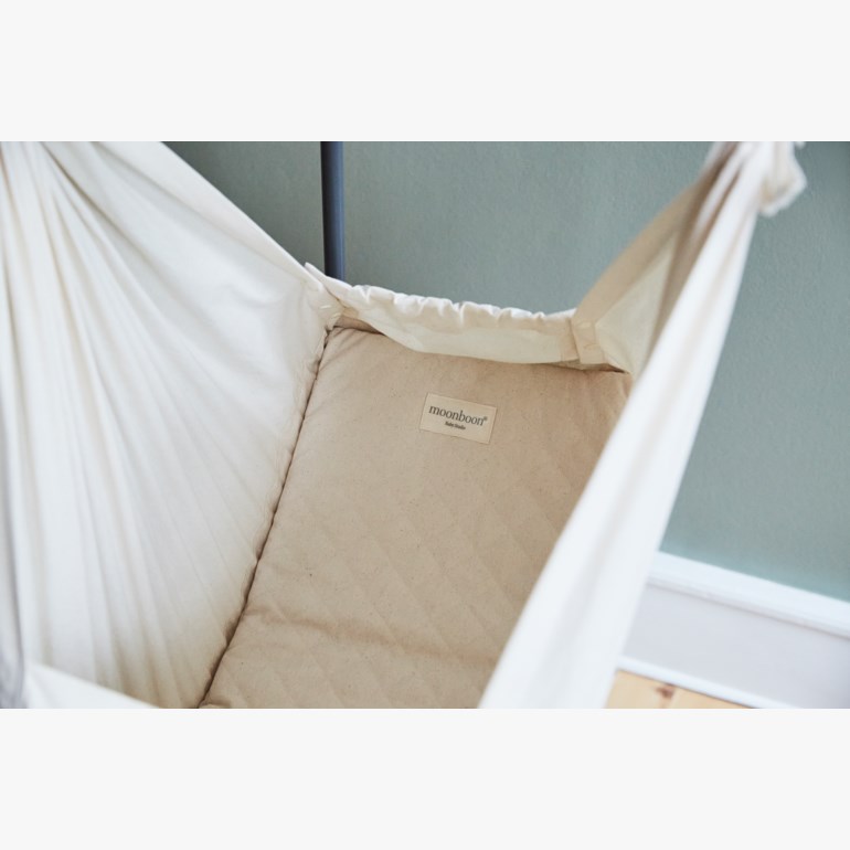 En lys beige babyvugge med vattert bunnplate og snøring i overkant.