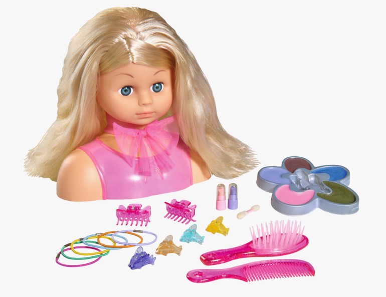 Blond dokke stylinghode med rosa topp og sløyfe, børste, kam, fargerike hårklemmer, hårstrikker, leppestifter og en blomstformet sminkepalett.