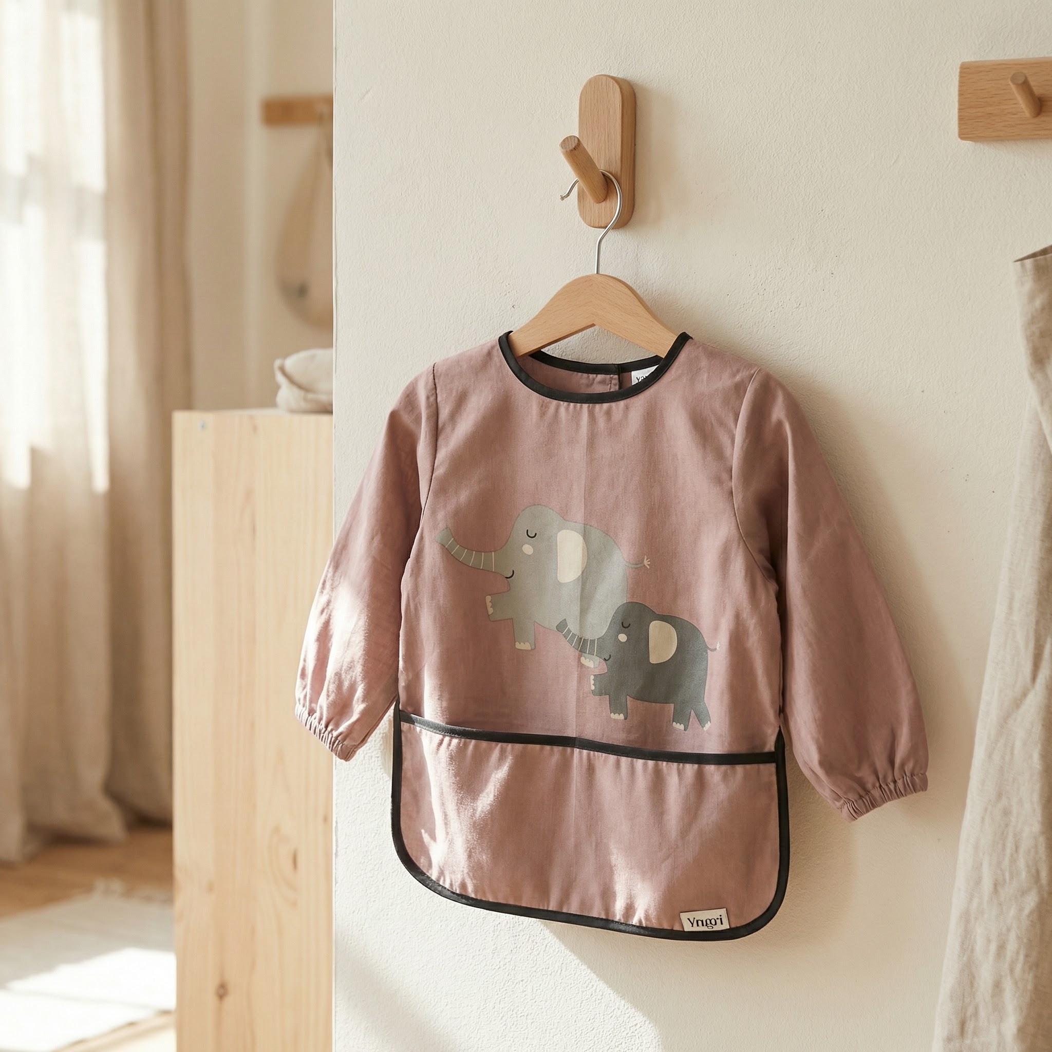 Støvrosa langermet baby smekke med grå elefanttrykk, svart kantbånd og elastiske mansjetter.