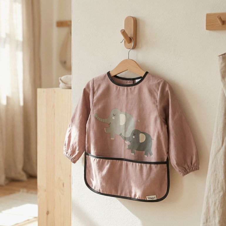 Støvrosa langermet baby smekke med grå elefanttrykk, svart kantbånd og elastiske mansjetter.