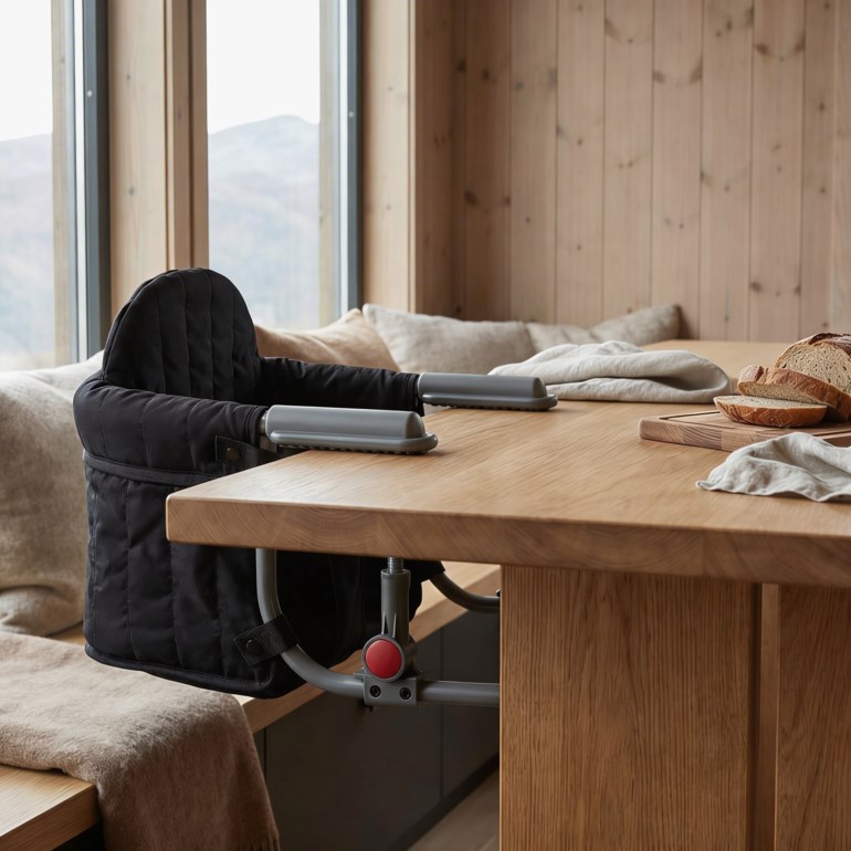 Svart klemmebabystol med en baby i lysebrun strikket cardigan og mønstrede beige og brune sokker.