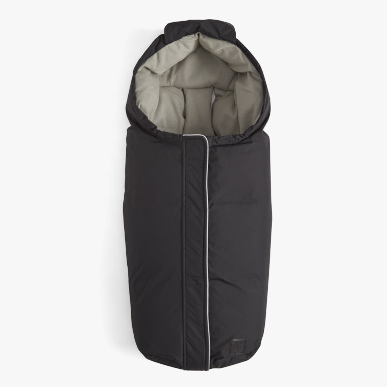 Svart babyvognpose med grå for, hette og hvitpipet glidelås foran, flat lay.