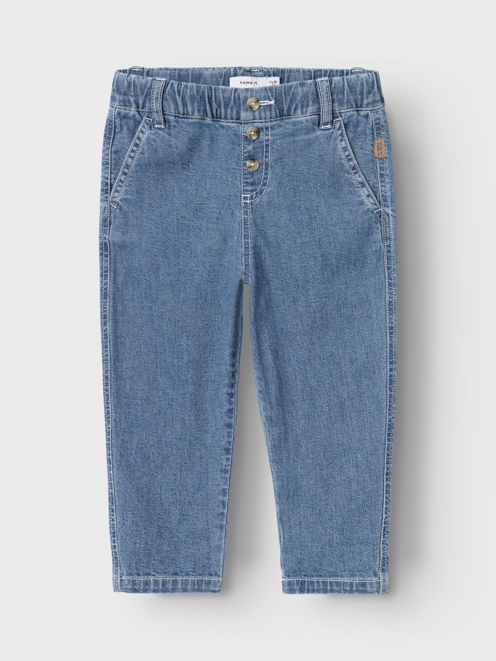 Frontvisning av lyseblå denimjeans for barn med elastisk midje, tre knapper og hvite kontrastsømmer.