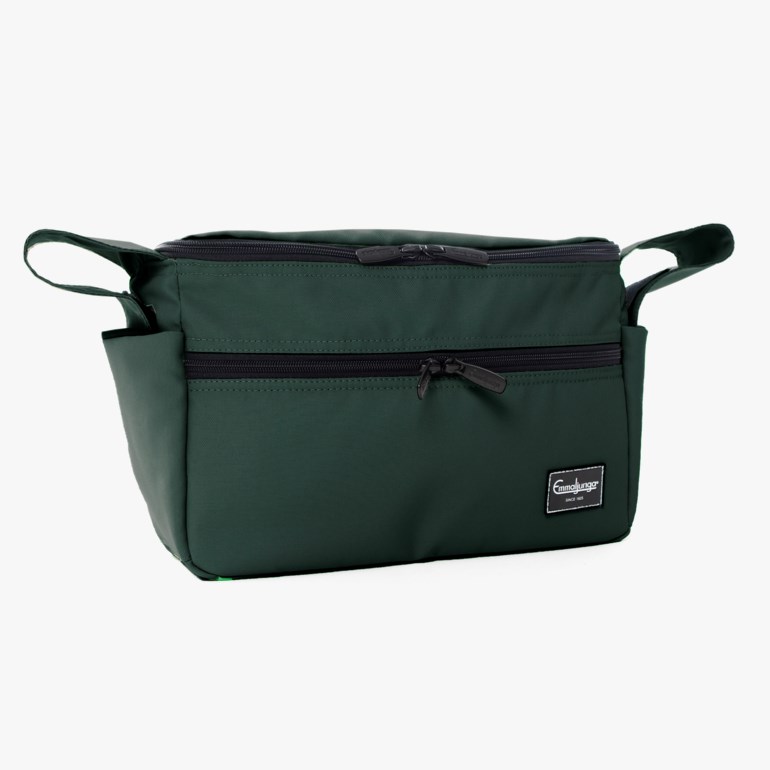 Mørkegrønn rektangulær veske med to glidelåser oppe, en glidelåslomme foran og sideløkker.