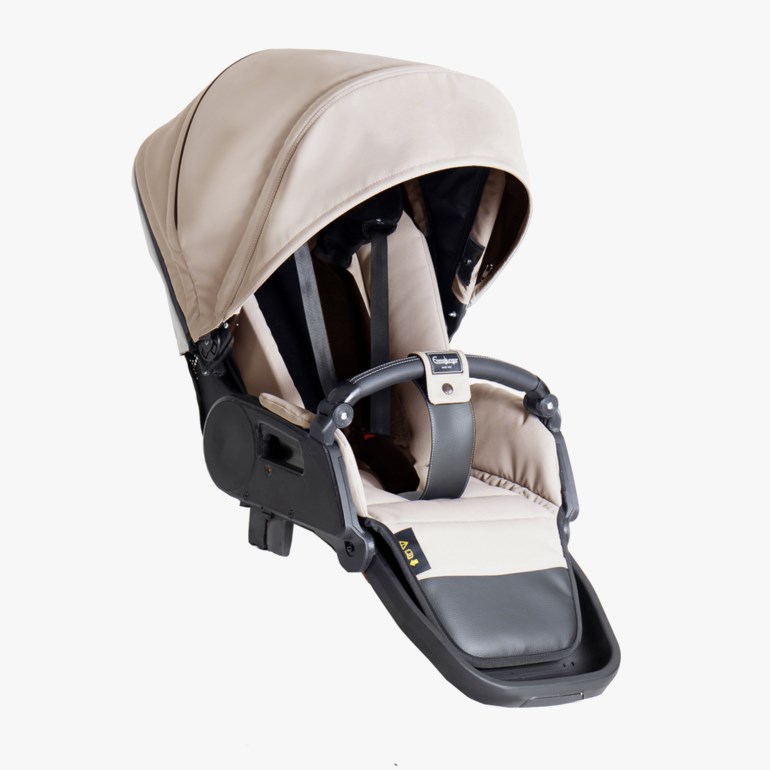 Beige og svart barnevognsete med kalesje, sele, bøyle og fotstøtte, forfra.