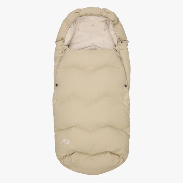 Beige polstret babyvognpose med glidelås, sidetrykknapper og mønstret innerfôr, forfra.