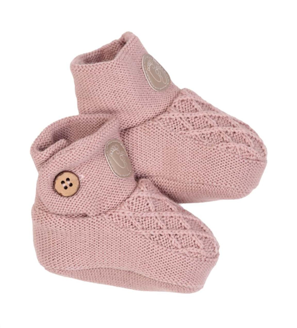 Et par rosa strikkede babytøfler med flettemønster, fotavtrykkmerke og treknappdetalj.
