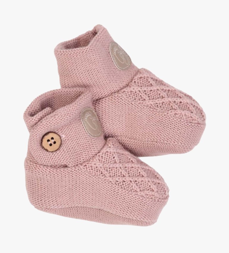 Et par rosa strikkede babytøfler med flettemønster, fotavtrykkmerke og treknappdetalj.