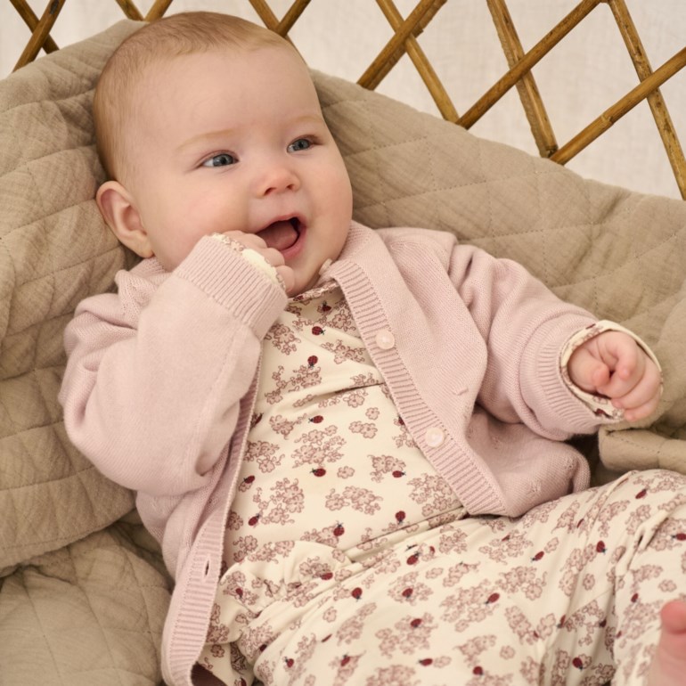 Baby i kremfarget todelt sett med blomstermønster og marihøner, med lysrosa cardigan.