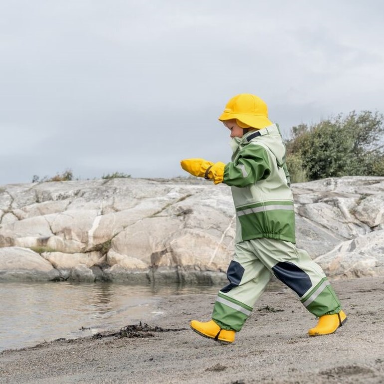 Barn har på seg et lys- og mørkegrønt regnsett med refleksstriper, gul hatt, votter og støvler.
