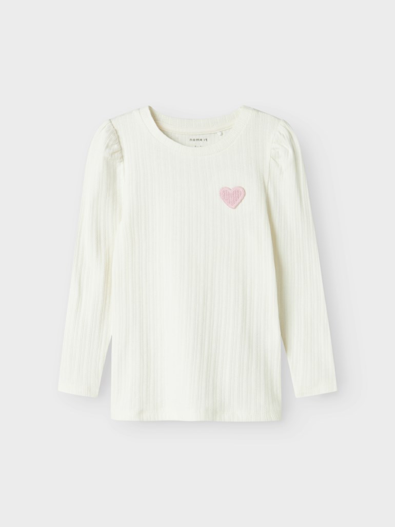 Barnets hvite ribbestrikkede langermede topp med puffermer og et rosa hjerteemblem på brystet, forfra.