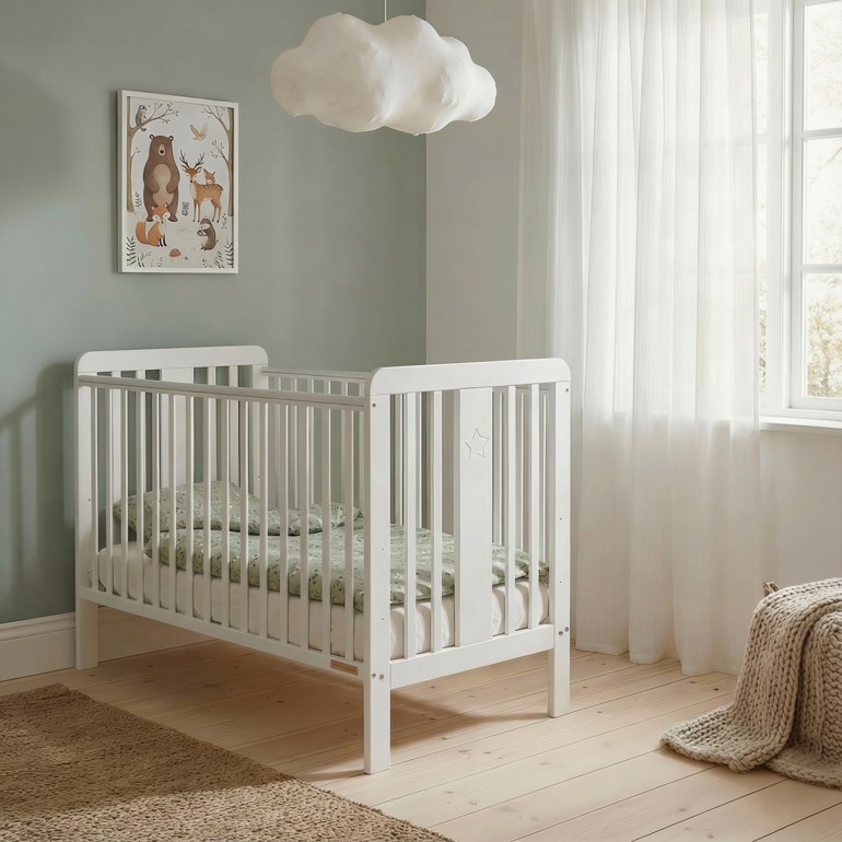 Hvit babyseng med stjerneutskjæring, grønne mønstrede sengetøy, brunt teppe og et beige strikket pledd.