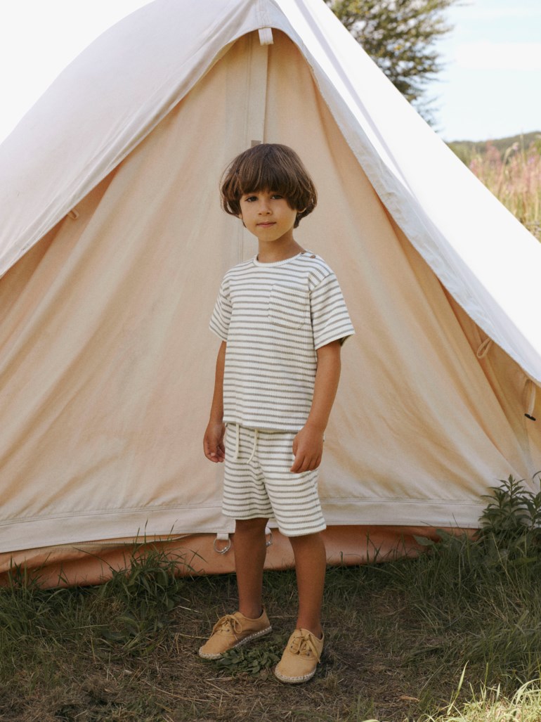 Barn har på seg en grønn og hvit stripete ribbet t-skjorte og matchende shorts med brune snøresko.