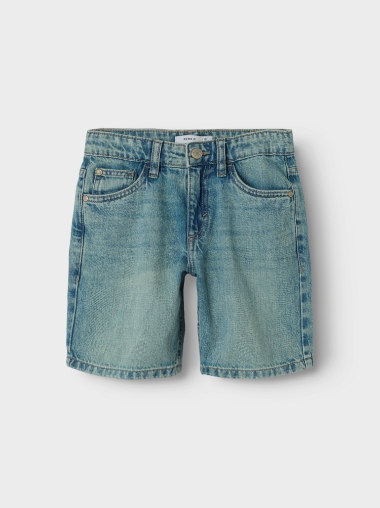 Barns lyseblå vaskede denimsorts med frontlommer og knappegylf, sett forfra.