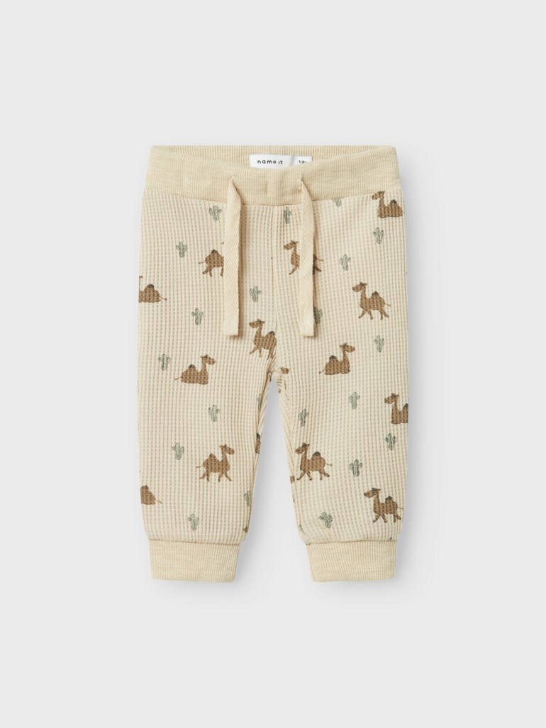 Lyse beige vaffelstrikkede babybukser med kamel- og kaktusmønster, snøring og elastiske mansjetter.
