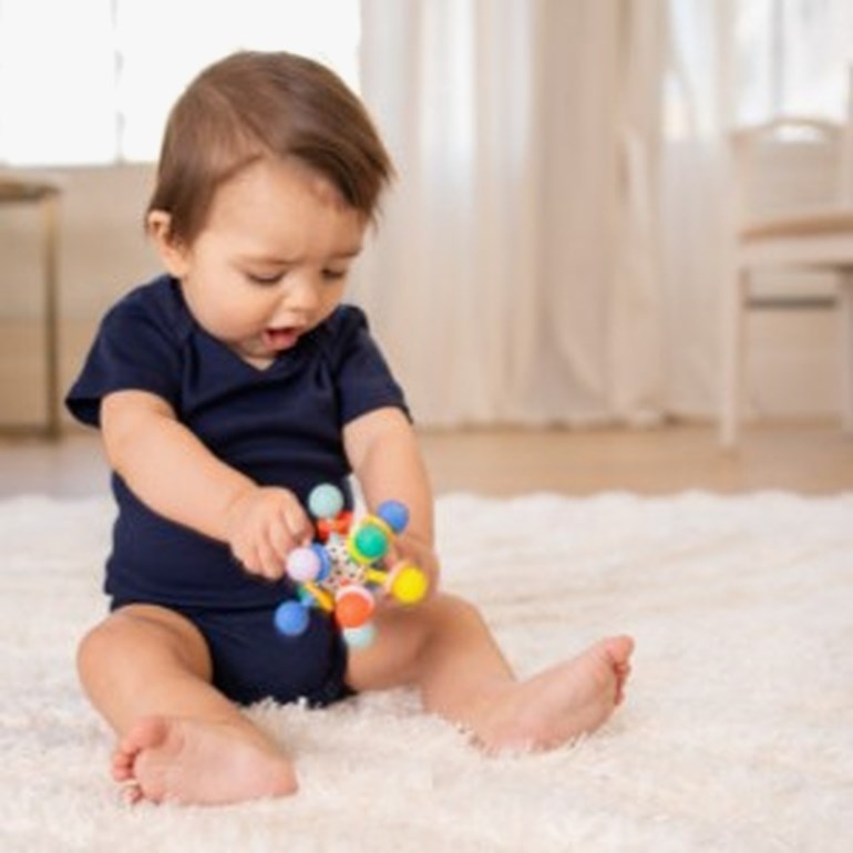 Baby bruker en marineblå kortermet body, holder en fargerik rangle.