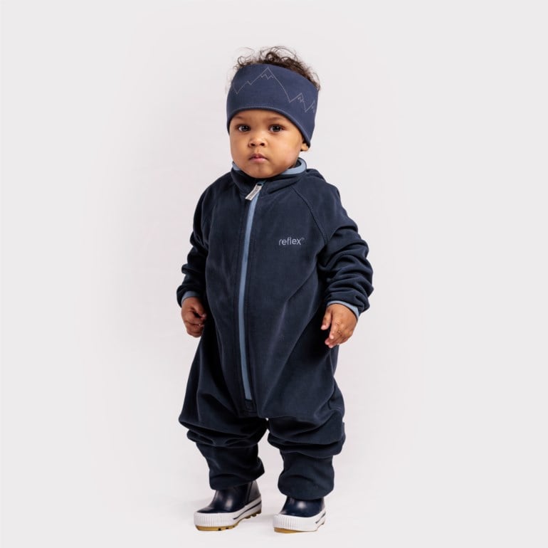 Baby har på seg en mørkeblå fleeceoverall med lyseblå glidelås, et matchende pannebånd med fjellmønster og mørkeblå støvler.