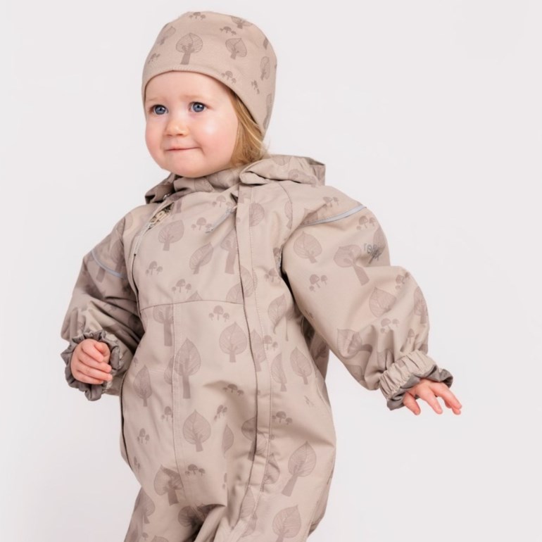 En baby har på seg en beige overall med blad- og sopptrykk, en hette og en matchende lue.
