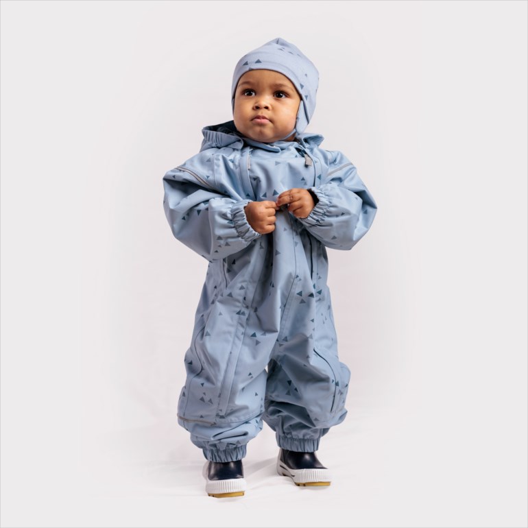 Baby i en lyseblå mønstret heldress med matchende lue og mørkeblå støvler.