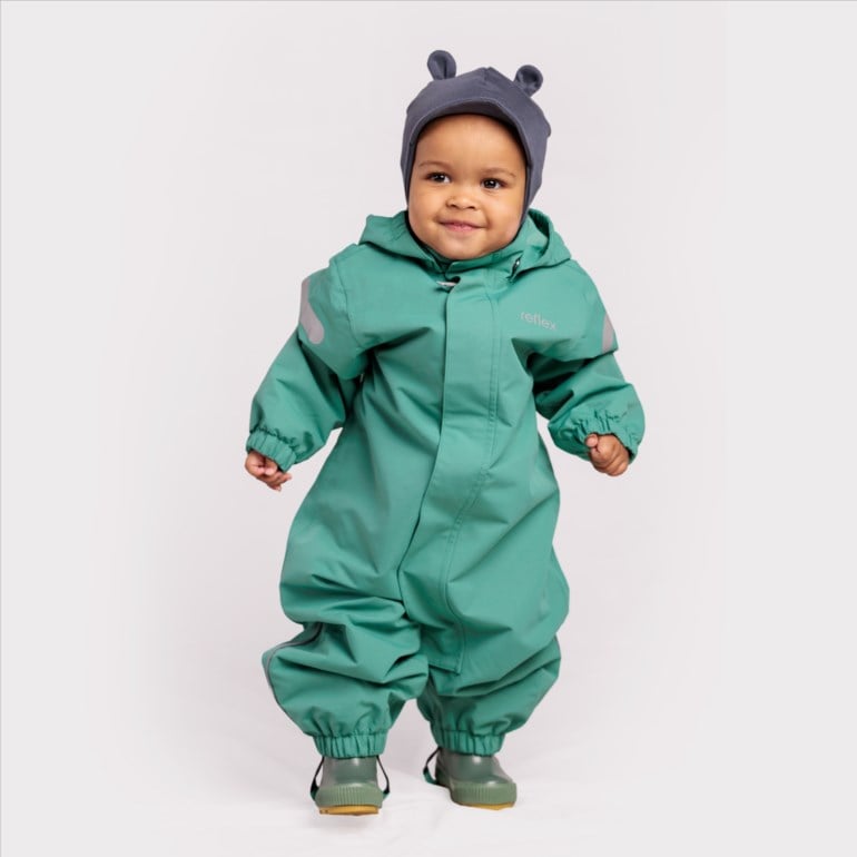 Baby har på en grønn regndress med hette og refleksdetaljer, en mørkegrå ørehette og grønne gummistøvler.