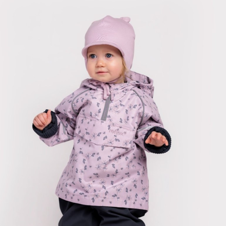 Baby har på seg en lilla blomstret anorakkjakke med mørke mansjetter, en rosa lue og mørke bukser.