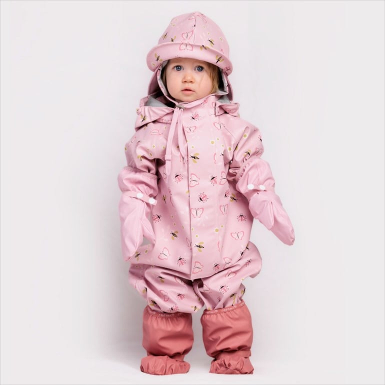 Baby har på rosa mønstret heldekkende regndress med matchende hatt, votter og støveltrekk, forfra.