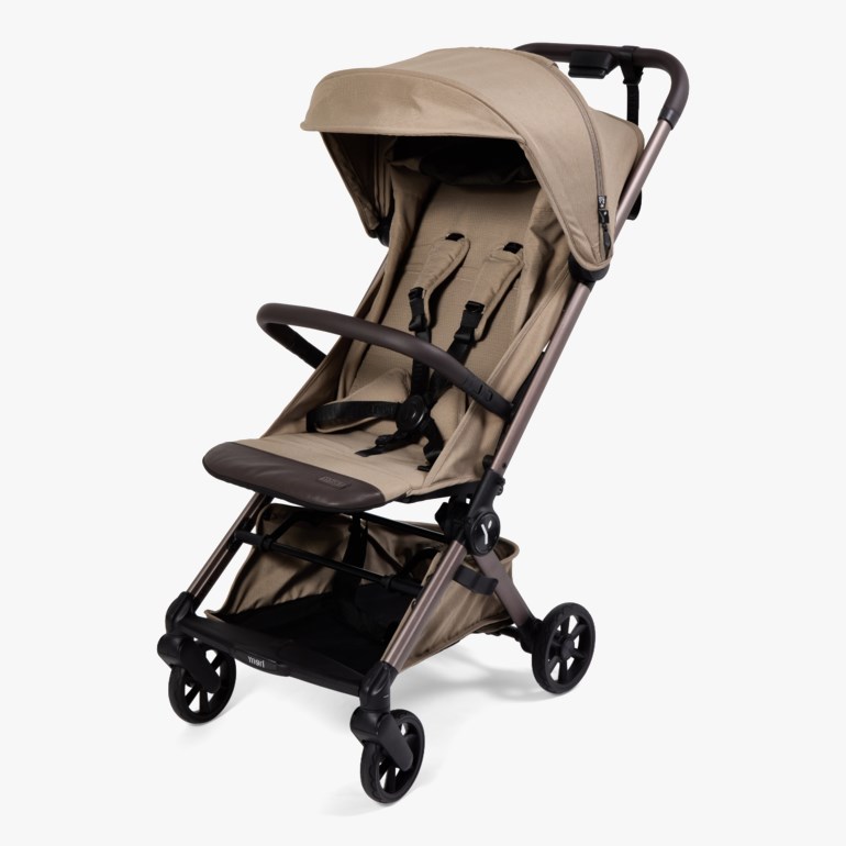 En beige barnevogn med bronsefarget ramme, mørkebrunt håndtak, bøyle og en oppbevaringskurv.