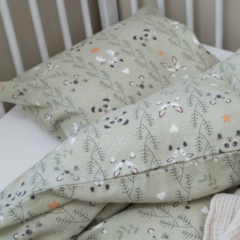 Lysegrønt baby påslakensett, putetrekk og beige teppe med skogsdyrmønster i sprinkelseng.