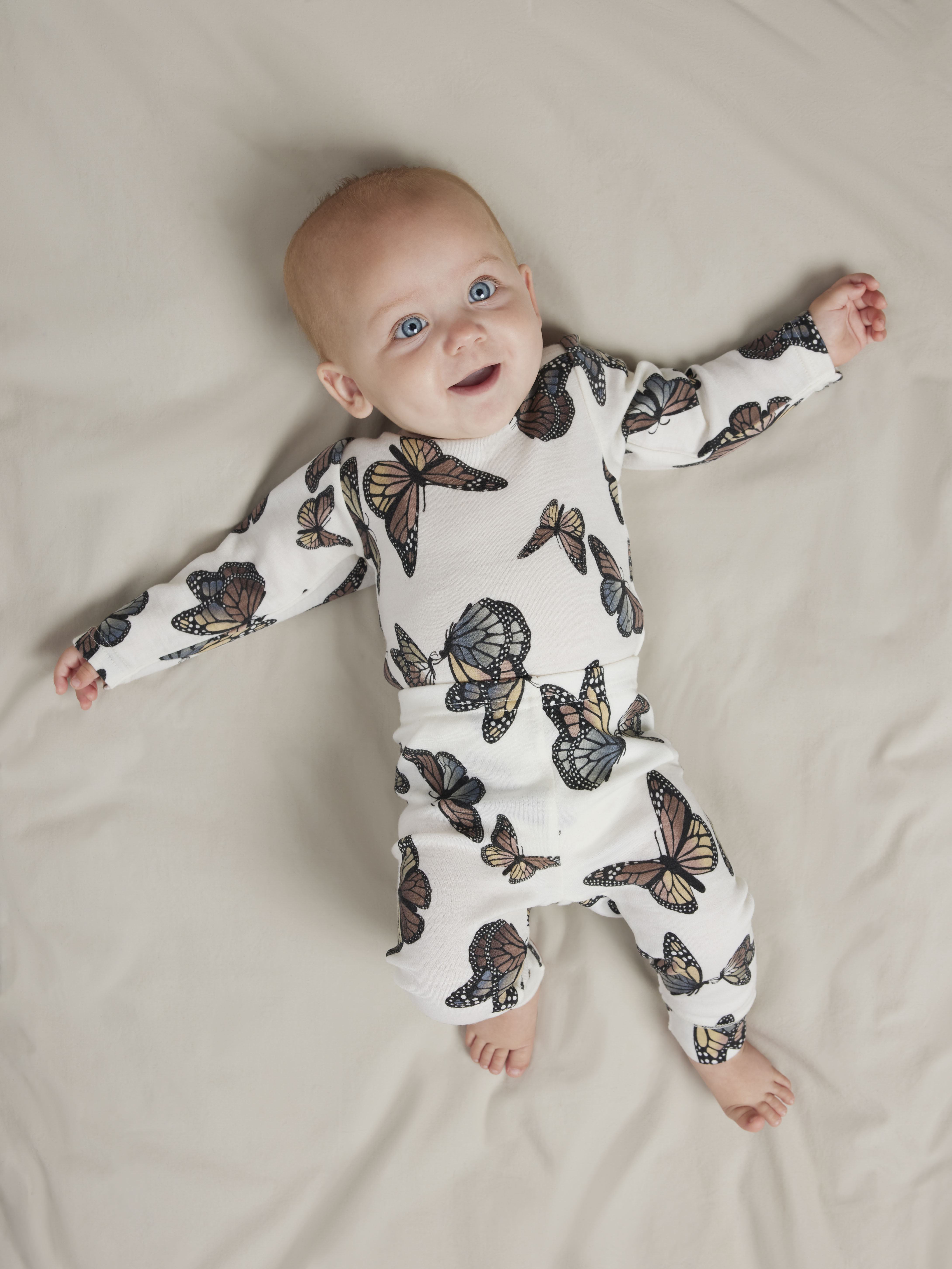 Baby har på seg en hvit langermet topp og matchende bukser med sommerfuglmønster, forfra.
