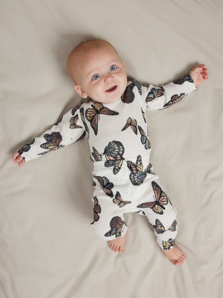 Baby har på seg en hvit langermet topp og matchende bukser med sommerfuglmønster, forfra.