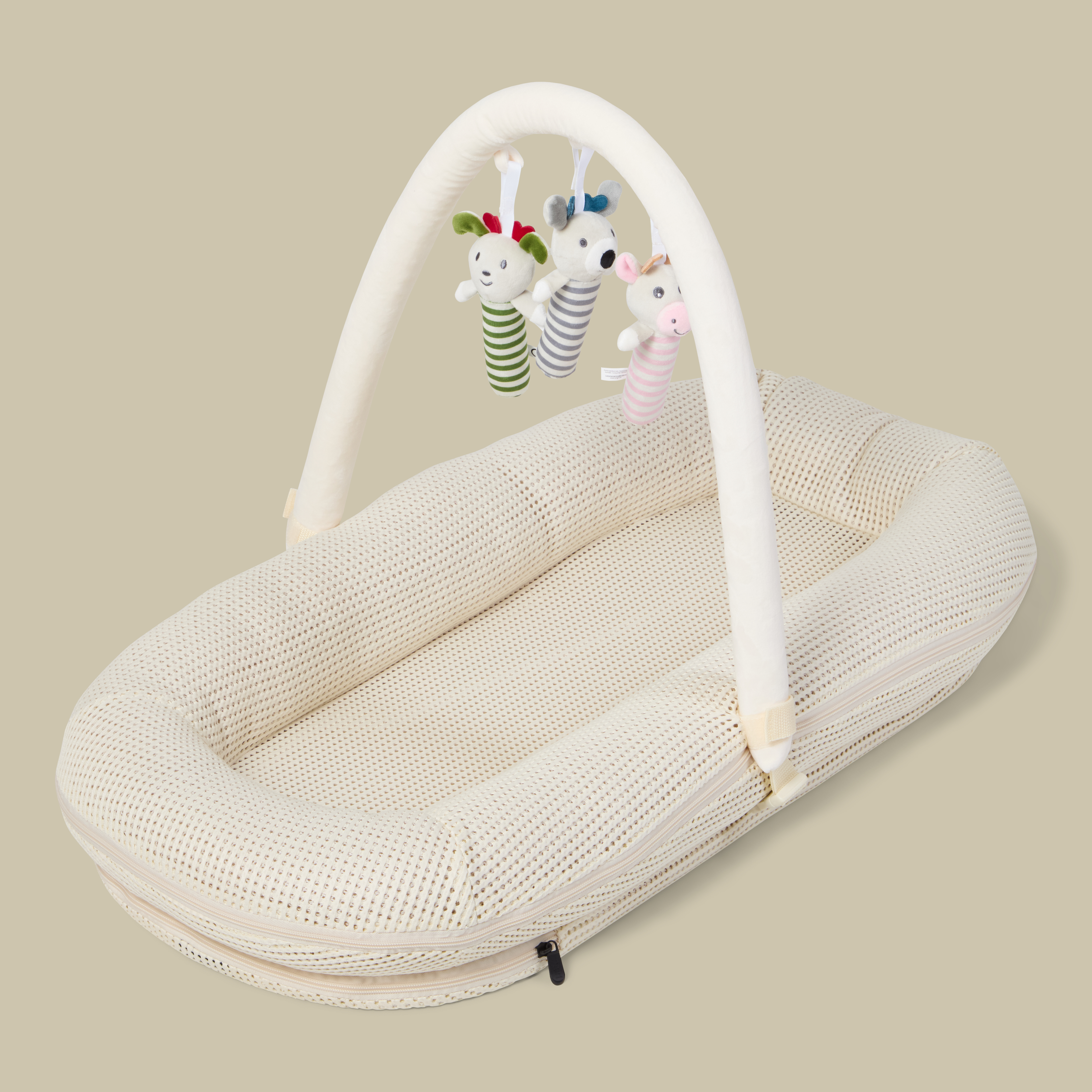 Beige babynest i meshtekstil med bue og tre hengende kosedyr-rangleleker.