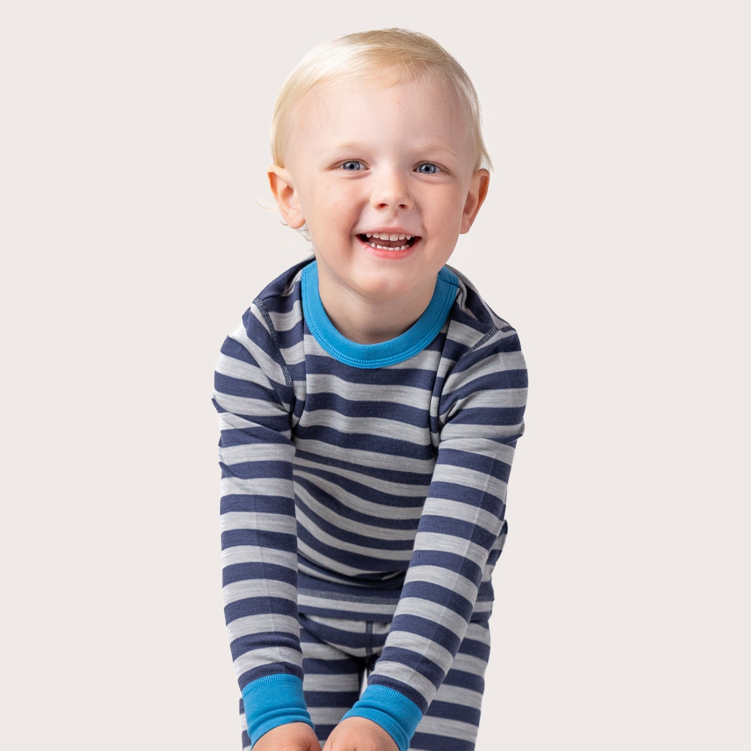 Barn har på blå og gråstripete langermet pyjamas med blå mansjetter og krage, forfra.