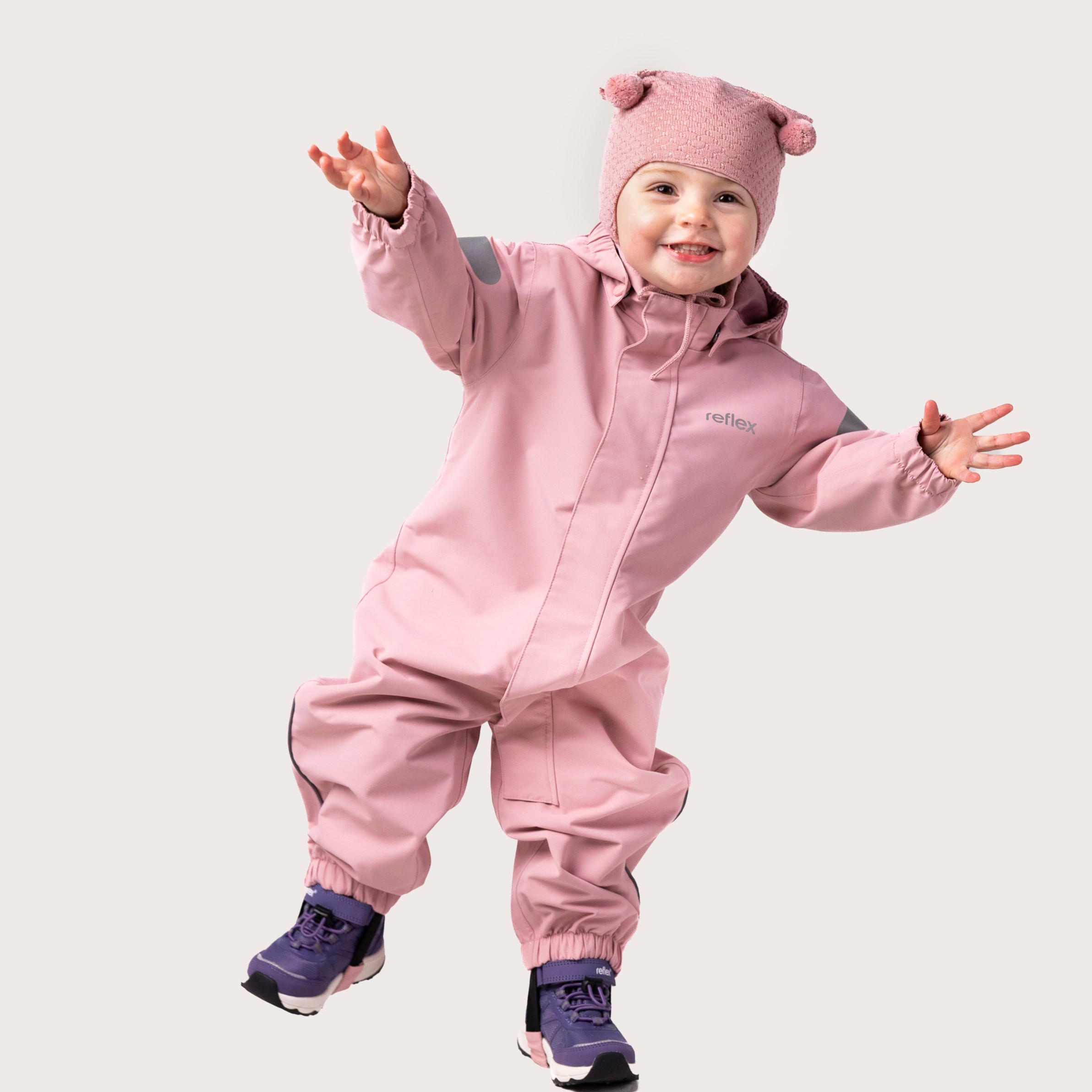 Barn har på seg en rosa hetteoverall med refleksdetaljer, en rosa strikkelue og lilla støvler.