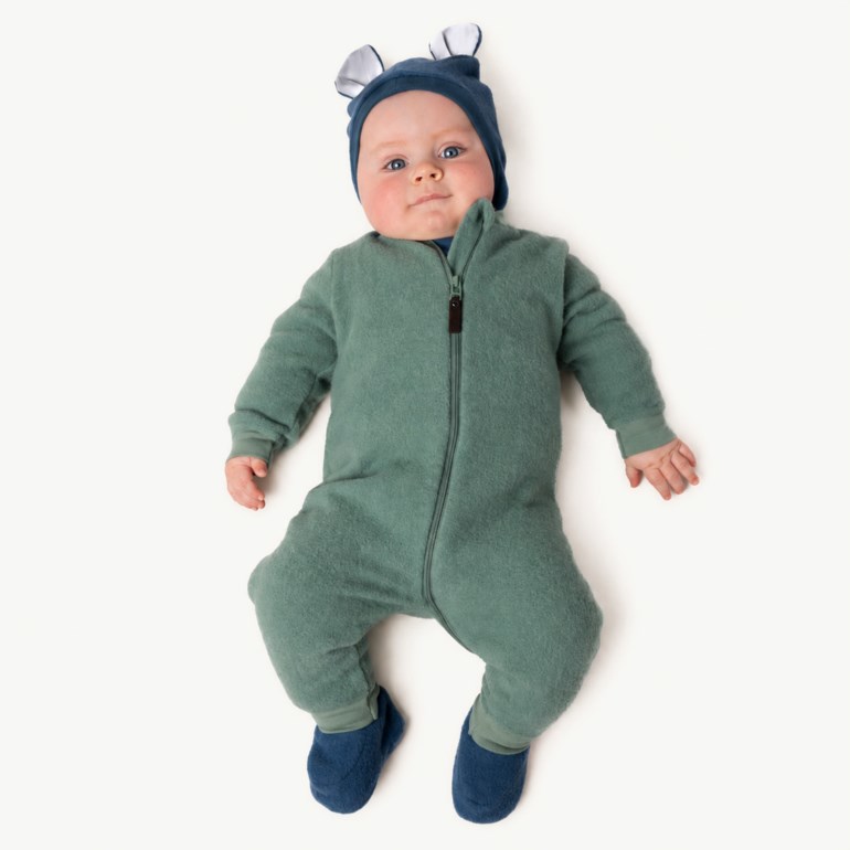 Baby i grønn ullfleece heldress med glidelås, mørkeblå lue med ører og mørkeblå tøfler.