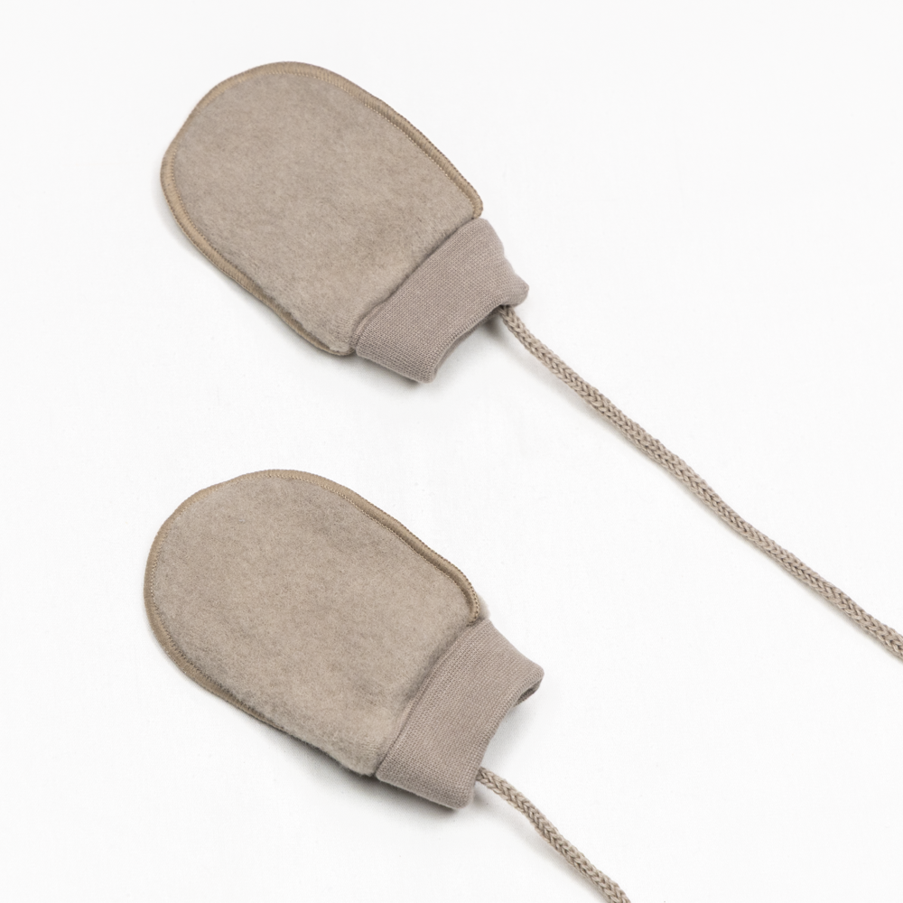 Et par beige babyvotter i filt med ribbestrikkede mansjetter, forbundet med flettet snor.