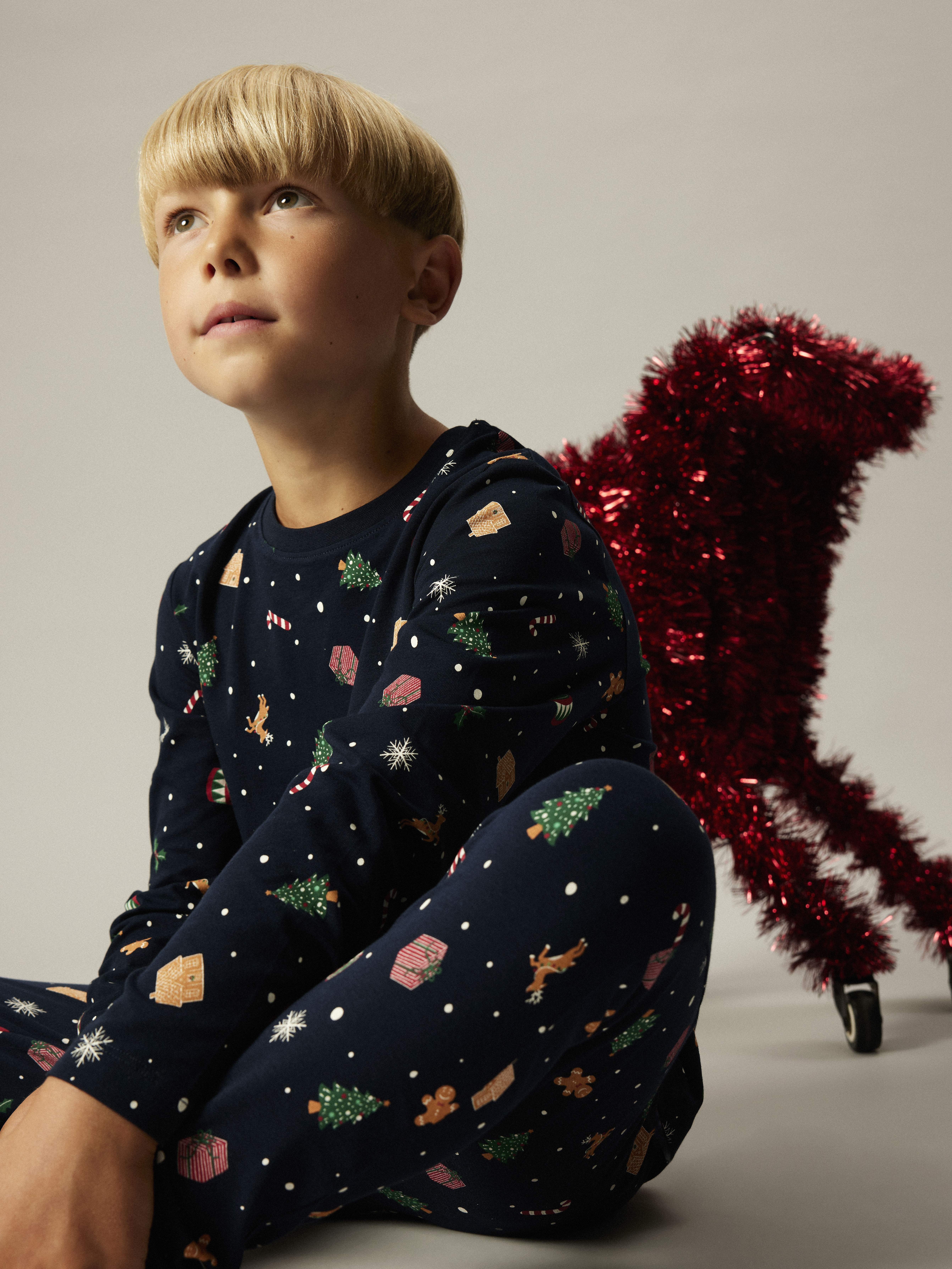 Barns mørkeblå langermet pyjamas med festlige julemønstre som trær, gaver og reinsdyr.