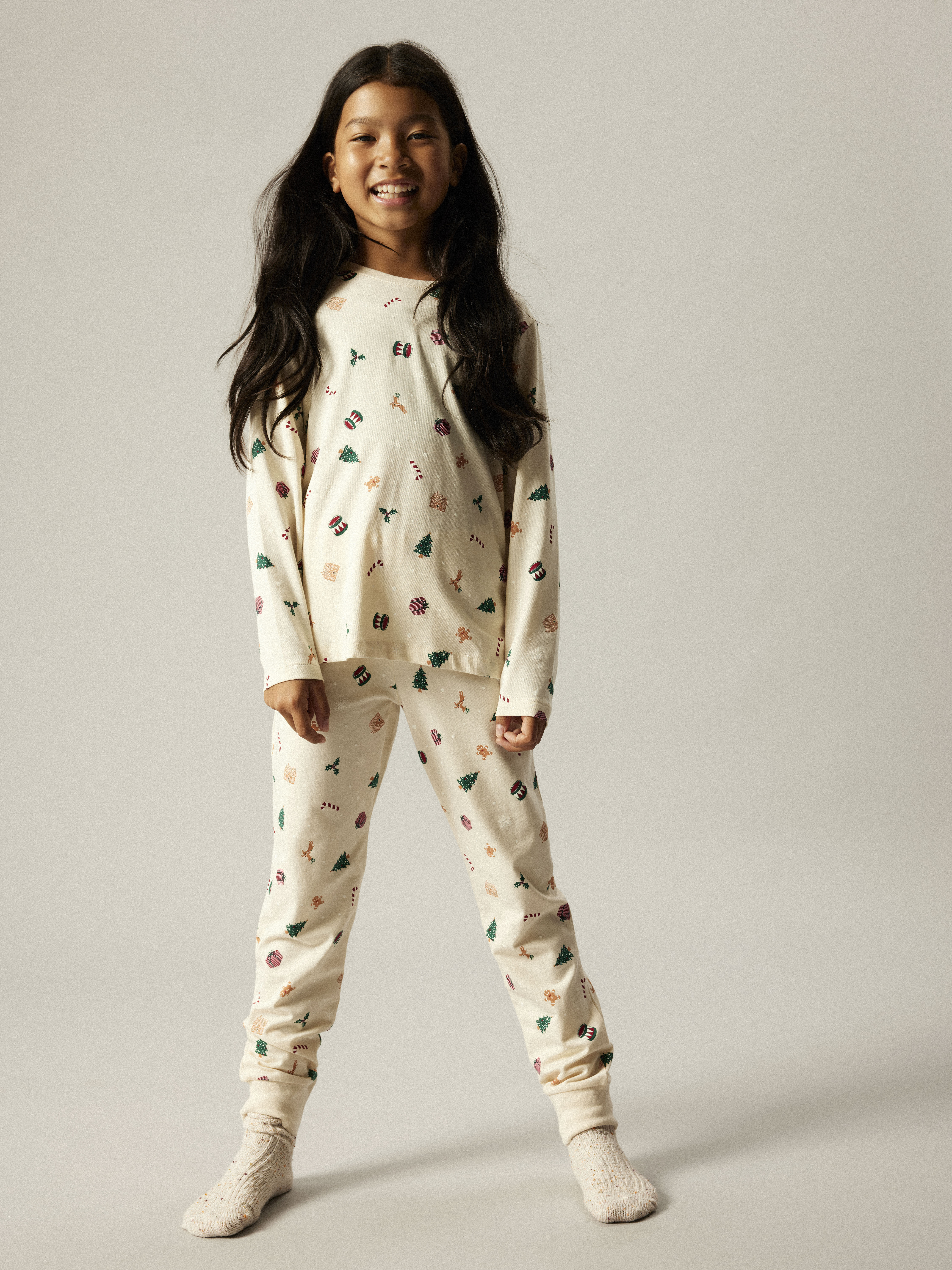 Barns kremfargede pysjamas-sett med julemønster, brukes med kremfargede sokker.