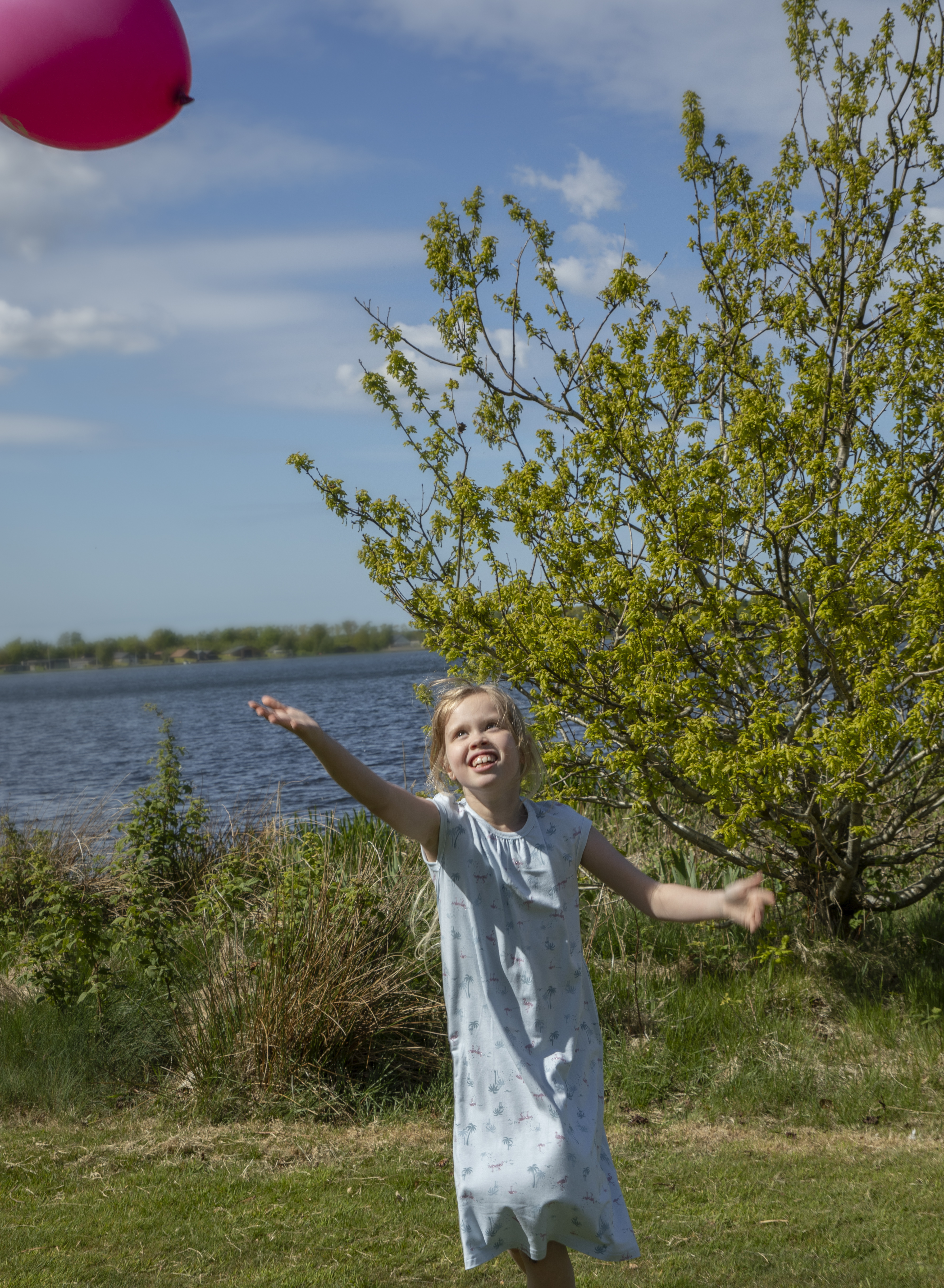 Jente i en lys blå kortermet knelang kjole med diskret palmemønster, sett forfra.