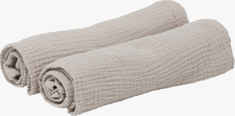 To lys beige teksturerte håndklær er rullet og plassert side om side.