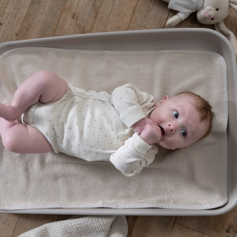 Baby i en lys beige ribbet langermet body med små hjertemønster.