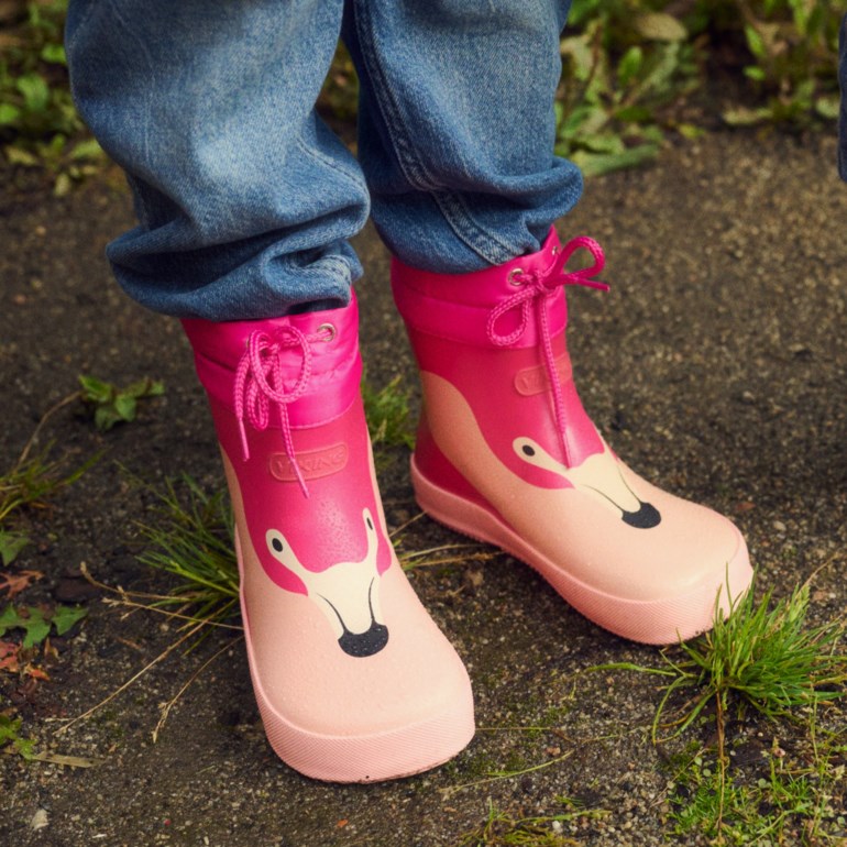 Rosa regnstøvler med flamingotrykk og snøring, kombinert med blå jeans på et barn.