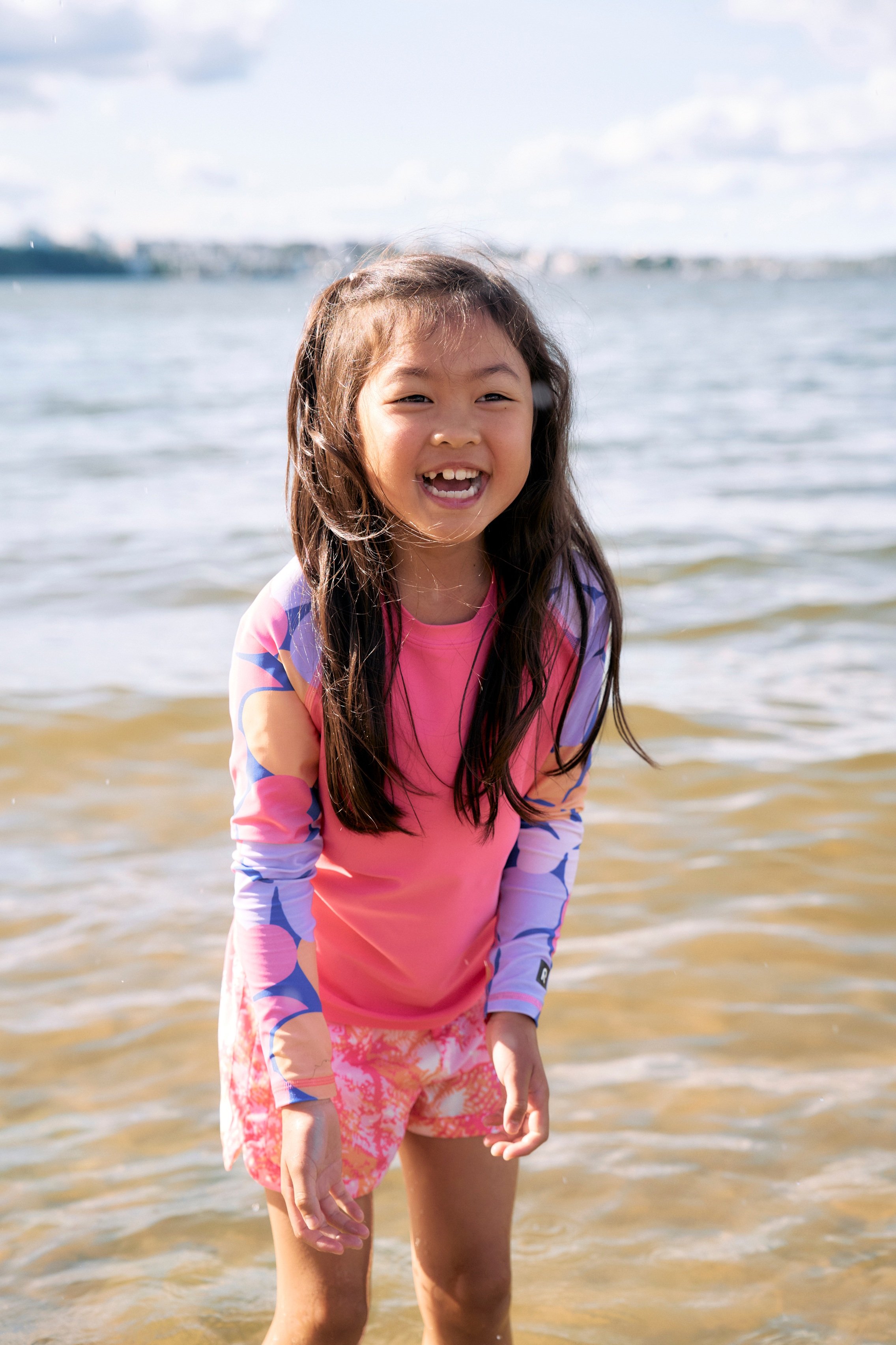 Barn i rosa rash guard med flerfargede mønstrede ermer og rosa mønstrede shorts, forfra.