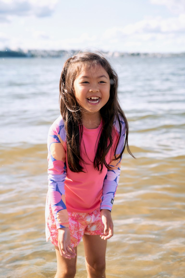 Barn i rosa rash guard med flerfargede mønstrede ermer og rosa mønstrede shorts, forfra.