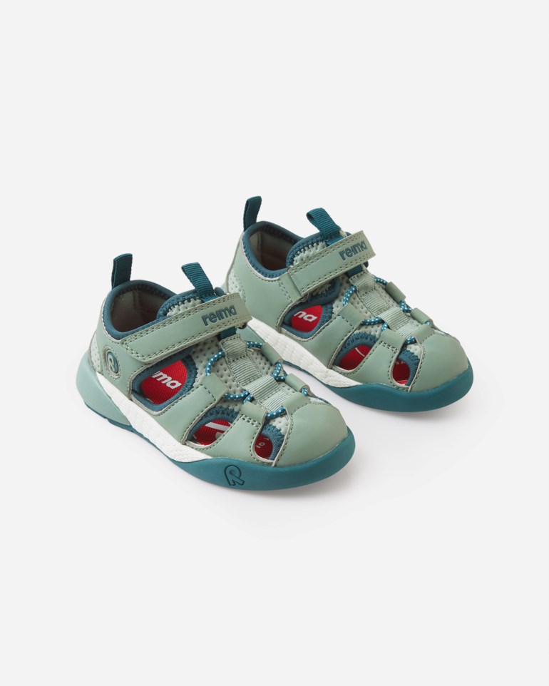 Et par grågrønne og mørkeblå barnesandaler med lukket tå, røde detaljer og hvite såler, forfra.