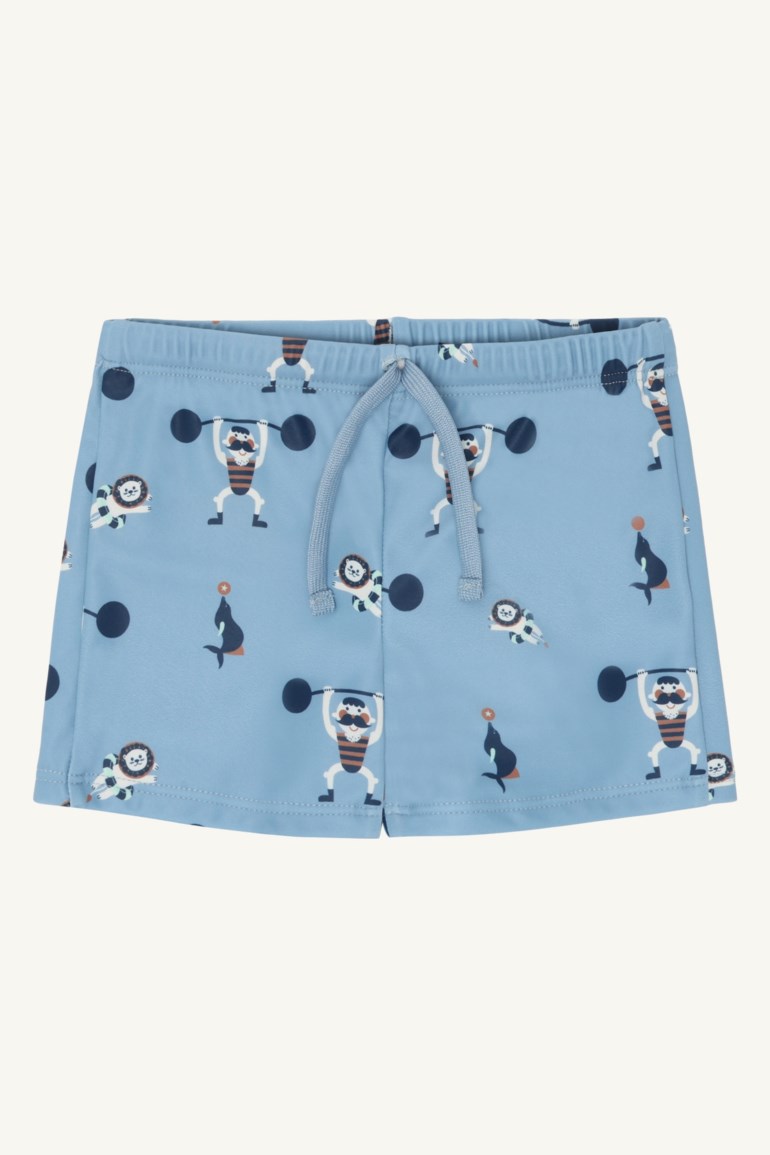Barnas lyseblå badeshorts med strikk i livet, snøring og gjentatt sirkusdyr- og sterkemannstrykk.